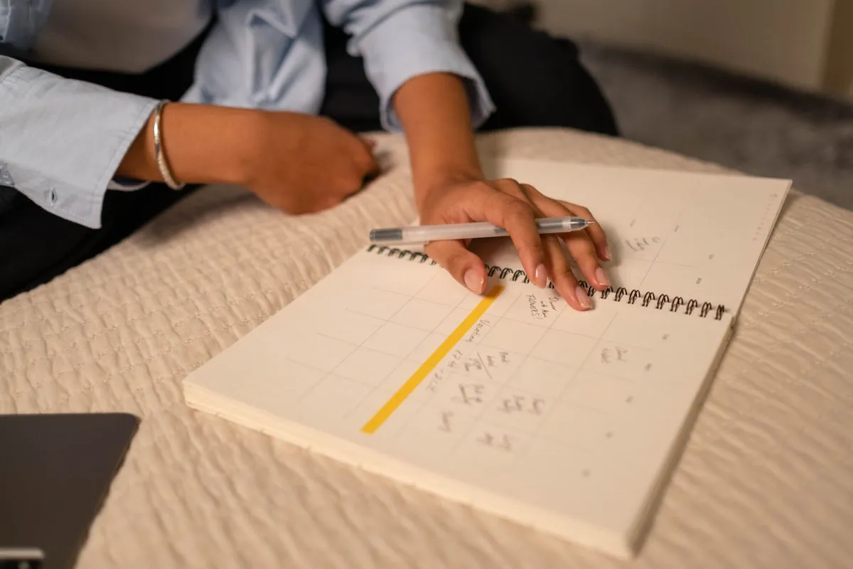 A hand marking a monthly planner during a weekly review, because recalibrating the plan down to what reality can hold is the layer everyone skips